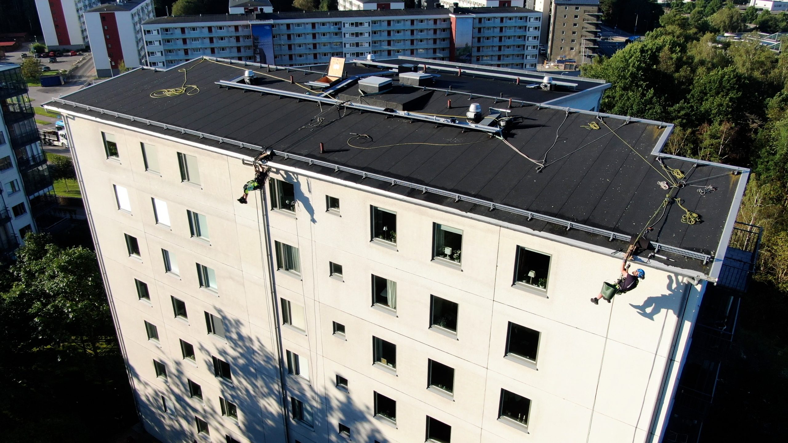 Flervåningshusfasad av BRF Musetten. Två personer utför höghöjdsarbete med rope access och hänger från rep